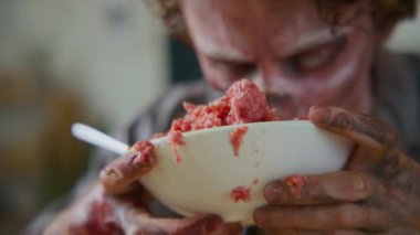 Kanlı, çürümüş eti çiğneyip çiğneyen, ağzı silen ve titreyen beyaz gözleriyle kameraya bakan aç erkek zombiye yakından bakmak.