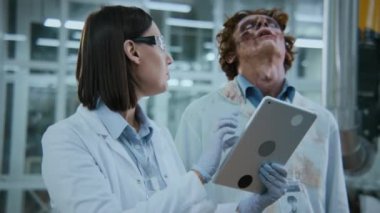 Kafkasyalı kadın bilim adamının tabletle orta ölçekli fotoğrafı araştırma verilerini tartışıyor ve sersemlemiş, hortlak gibi gezinen zombi bir erkek meslektaşla karşılaşıyor.