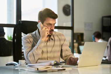Cep telefonuyla konuşan ve dizüstü bilgisayar kullanan kendinden emin genç erkek yönetici ya da işletme müdürü