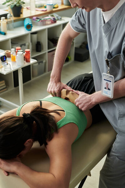 Хорошо обученный массажист, выполняющий терапию клиентам в спокойной обстановке в комнате для процедур. Эфирные масла, полотенца и оборудование видны на заднем плане