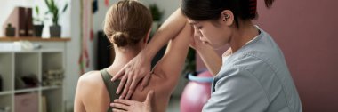 Fizyoterapist, arka planda çeşitli rehabilitasyon ekipmanlarıyla klinik ortamında hastaların omzuna ustaca masaj yapıyor.