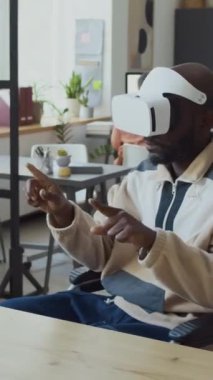 VR kulaklık takan, internette gezinen veya sanal gerçeklikte dijital belgelere bakan siyahi erkek geliştiricinin orta boy dikey görüntüsü.