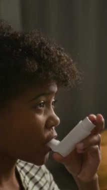 Kıvırcık saçlı ve astım tedavisi için astım ilacı kullanan Afro-Amerikan çocuğun dikey yakın çekimi.