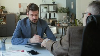 Male employee listening to CEO commenting on his business project, then putting on clown wig and nose while getting fired or pissed off at work in office