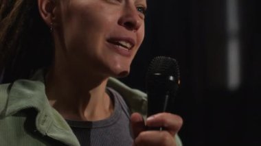Kafkas kız stand-up komedyeninin koyu yeşil tişört ve eflatun tişört giyip şakalar yaptığı, gülümsediği ve seyircilere baktığı yakın plan çekimleri.