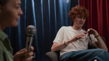 Beyaz kadın stand-up komedyeni ve kızıl saçlı sanatçının değişen odak noktasıyla çekilen çekim kulüpte izleyicilerle iletişim kurarken, sahnede sandalyelerde otururken aktif olarak şaka yapıyor.
