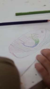 Küçük çocukların masada otururken kalemlerle çizim yaptıkları dikey bir fotoğraf.