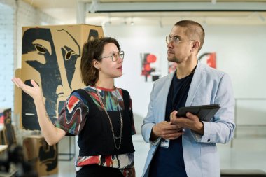 Sanat eserleri düzenlemesi vizyonunu dile getirmek ve sergiye hazırlanmasına yardım ederken galeri müdürüyle konuşan yaratıcı sanatçı