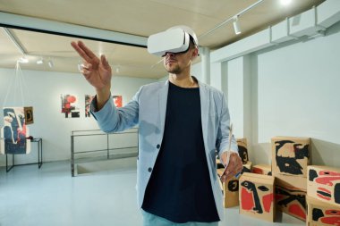 Zarif mavi takım elbiseli ve VR kulaklıklı genç adam interaktif modern sanat sergisi listesine bakıyor.