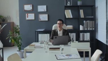 Orta yaşlı kadın yönetici, masadaki dizüstü bilgisayarda çalışıyor ve erkek doktorları selamlıyor, sağlık ofisine giriyor ve toplantı masasında oturuyor.