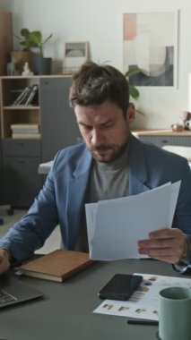 Odaklanmış ofis çalışanının dokümanları incelerken, masada dizüstü bilgisayar kullanırken, sandalyeye yaslanırken ve ara verirken dikey görüntüleri.