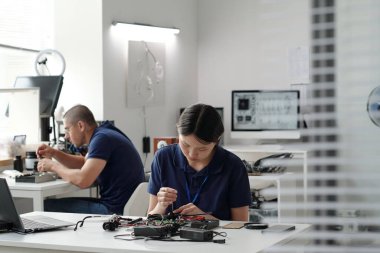 Kontrollü bir laboratuvar ortamında elektronik bileşenlerle çalışan mühendisler, teknolojik aygıtlar ve ekipmanlarla çevrili ayrıntılı ve hassas görevlere odaklanıyorlar.