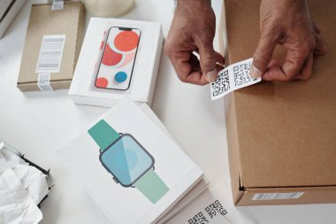 Akıllı telefon paketi ve akıllı kaset kutusu da dahil olmak üzere ambalaj malzemeleri ve teknolojik cihazlarla çevrili nakliye kutusunda etiketli QR kodu taranıyor