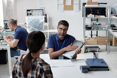 İki insan dizüstü bilgisayarlarını tutarken tartışırken toplantı modern ofis çalışma alanında gerçekleşiyor. Teknik cihazlar ve ofis malzemeleri arka planda görünür.