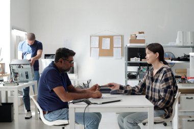 Modern ofis ortamında elektronik aletlerle işbirliği yapan insanlar. Kadın ve erkek cihazları değiş tokuş ederken, arka planda teknolojiyle çalışan başka bir kişi...