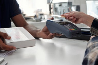Bir perakende mağazasında kart okuyucu kullanılarak yapılan ödeme işlemi sırasında el ele tutuşmalar. Ödeme için kart veren kişi, arka planda kutular ve depolama ürünleri ile