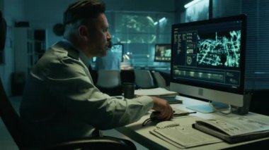 Kafkas erkek istihbarat subayı bilgisayarın önünde oturmuş şüpheli hareketler için uydu görüntülerini izliyor ve taşınabilir telsizden rapor veriyor.