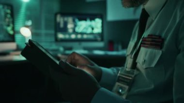 Tablette keşif sistemini yöneten, saha operasyonları ofisinde tek başına çalışan, üniformalı, orta yaşlı, beyaz erkek ajanın orta boy fotoğrafı.