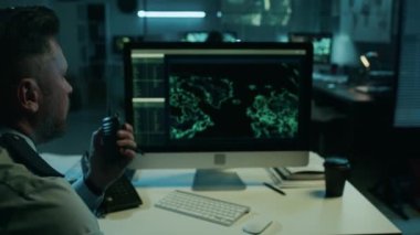 Kafkas erkek gözetleme memurunun gece bilgisayar ekranındaki görüntülerinin orta omuz üstü görüntüsü. Sonra da kritik güvenlik sorununu telsiz kumandanına bildirin.