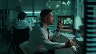 Kafkas erkek askeri uydu keşif subayı gece operasyon merkezinde çalışırken, bilgisayardaki uydu görüntülerini izlerken, taşınabilir radyodaki iş arkadaşlarıyla konuşurken orta ölçekli görüntüler.