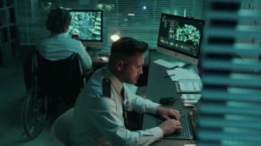 Üniformalı çeşitli erkek askerlerin orta boy fotoğrafı ve tekerlekli sandalyedeki kadın meslektaşın operasyon merkezindeki masalarda oturup gece vardiyası sırasında bilgisayarlardaki izleme sistemlerini izlemesi.