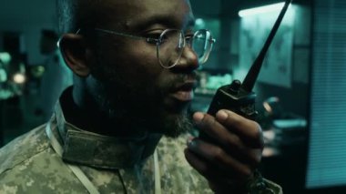 Kendine güvenen, kamuflaj üniformalı genç Afro-Amerikan teğmenin, uydu izleme merkezinde dikilirken taşınabilir telsizden düşman koordinatlarını ileten yüzü.