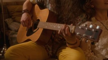 Kafkasyalı uzun saçlı ve bantlı beyaz adamın akustik gitar çalarken yakın çekimde, sevgili kız arkadaşı omzuna yaslanmış, neşeli yüzüyle müzik dinlerken.