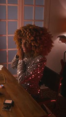 Dikey çekimde, parlak gümüş elbiseli, kabarık saçlı, bayan Afro-Amerikan ünlülerin konsere hazırlandığı, büyük küpeler taktığı bir sahne.