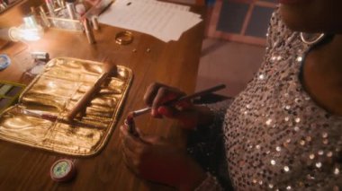 70 'lerin genç Afro-Amerikan bayan ünlülerinin yan çekimleri. Parlak, gümüş rengi elbiseli, parlak saçlı. Konserden önce aynanın önüne kırmızı ruj sürmek için fırça kullanıyor.