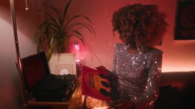 Havalı saçlı, parlak gümüş elbiseli, neon ışıklı odada 70 'li yılların plak plaklarını çalan modaya uygun, genç, Afro-Amerikan disko yıldızının orta ölçekli resmi.