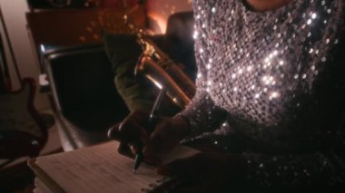 70 'li yaşlarda neon ışıklı sanatçılar odasında şarkı yazarken kanepede oturan parlak gümüş elbiseli genç Afrikalı kadın şarkıcının yakın çekim görüntüleri.