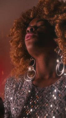 70 'lerin düşük açılı genç siyahi disko yıldızı, kabarık saçlı, gümüş parıltılı elbisesi ve büyük küpeleri olan, yeni şarkı sözleri besteleyen ve sanatçı odasında not defterine yazan.