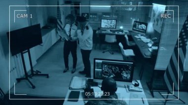 Çok ırklı erkek ve kadın ordu mensuplarının güvenlik dosyalarını tartışarak, uydu gözetleme verilerini analiz ederek operasyon merkezinde birlikte çalışmalarını gösteren yüksek açılı kamera görüntüleri.