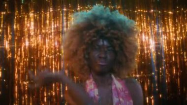 Aktif ve karizmatik, kıvırcık saçlı, renkli açık elbiseli, parlak kolyeli, süslü arka planda dans eden ve kulüpte eğlenen Afro-Amerikan bayanın portresi.