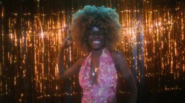 Kabarık saçlı, renkli bir hippi elbisesi giyen, 70 'li yıllarda kulüpte ışıltılı ve karizmatik bir şekilde dans eden Afro-Amerikan bir kadının orta boy portresi.