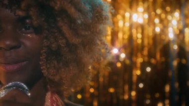 Kabarık saçlı, mikrofona şehvetli bir şekilde şarkı söyleyen genç siyahi kadın şarkıcının gece kulübündeki parlak altın sarısı arka plan, nostaljik 70 'ler, fotokopi alanı.