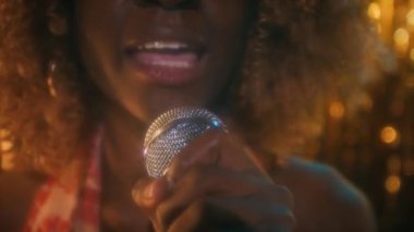 Kendine güvenen, kabarık saçlı, mikrofona şehvetli bir şekilde şarkı söyleyen, yüzünde parıltılar olan, kulüpteki parlak arka planda, kameraya bakan, 70 'li yaşlarda,