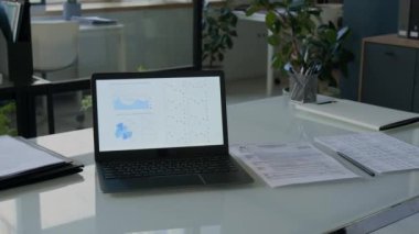 Modern ofiste finansal veri grafiklerini, kalemlerini ve belgelerini gösteren dizüstü bilgisayarlı bir masa.