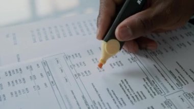 Analiz sırasında finansal belgelerdeki önemli rakamları işaretlemek için fosforlu kalem kullanan tanınmayan bir işadamının yakın plan fotoğrafı.