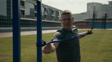 Aheiria sendromlu, orta karar beyaz sporcunun stadyumda direnç bantlarını bağlayıp göğüs kaslarını çalıştırırken bir kolunu uzatarak yarışmaya hazırlandığı bir fotoğraf.