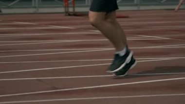 Siyah şortlu ve spor ayakkabılı tanınmayan bir sporcunun, güneşli yaz mevsiminde açık hava stadyumunda koşan orta boy yavaş çekimleri.