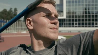 Mızrak tutan yakışıklı, yakışıklı, beyaz bir sporcunun yüzüne yakın çekim, atmayı hedefliyor, sonra tutuşu ayarlıyor, atletizm stadyumunda tekniği geliştiriyor.