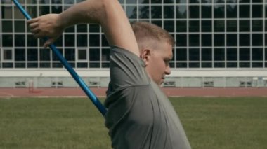 Açık hava stadyumunda cirit atmadan önce vücut kaslarını esneten akheiria engelli, enerjik, genç beyaz erkek sporcunun orta boy yakın çekimi.