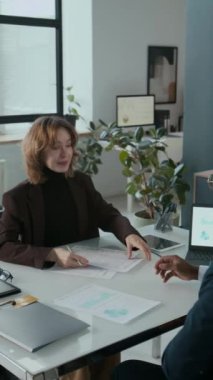 Genç bir kadının anlaşma imzalarken, kredi kartıyla belgeler alırken ve ofis toplantısı sırasında mali danışmanla el sıkışırken dikey çekimi.