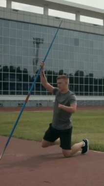 Kafkas erkek para sporcusunun tam dikey çekimi. Uzuvları farklı, diz çökmüş ve vücut kaslarını cirit atarak geriyor. Yaz günü koşu ve saha eğitim tesisinde.
