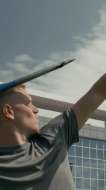 Orta boy beyaz erkek para atleti atletizm antrenmanı yaparken orta dikey olarak arka planda, nişan alıyor, cirit atıyor ve şampiyonluğa hazırlanırken onu seyrediyor.