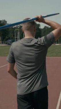 Özürlü, engelli, yeşil alana doğru yürüyen, omuz üzerinde cirit atan, antrenman yapmak için konsantre olan orta boy erkek para-atletin tam dikey arka çekimi.