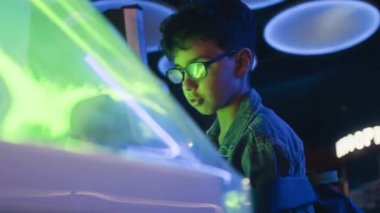 Eğlence atari salonunda, neon ışıklarda, hafta sonları takılırken aynı anda sakız çiğneyen, odaklanmış, meşgul Hintli genç çocuğun orta açılı yakın çekimi.