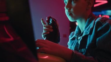 Eğlence merkezinde oturmuş, joystick kullanarak uçuş ya da yarış simülatörü oyunu oynarken sakız çiğneyen 12 yaşındaki sıradan kot ceketli Hintli çocuğun orta boy yakın çekimi.