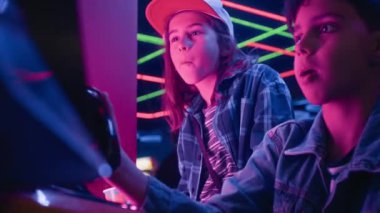 Orta yaşlı Orta Doğulu bir çocuğun oyun salonunda oyun oynarken, oyun çubuğuyla sakız çiğnerken, beyaz bir arkadaşın izlediği ve geçtiği seviye için tavsiye verdiği orta boy bir fotoğraf.